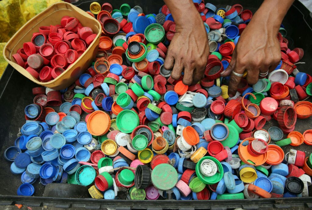 Blogs A vibrant assortment of plastic bottle caps being sorted by hand for recycling in Manila.