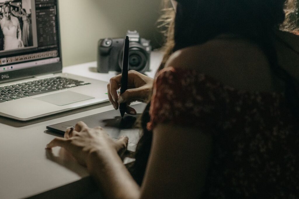 A woman uses a graphic tablet and laptop for photo editing in a modern workspace.